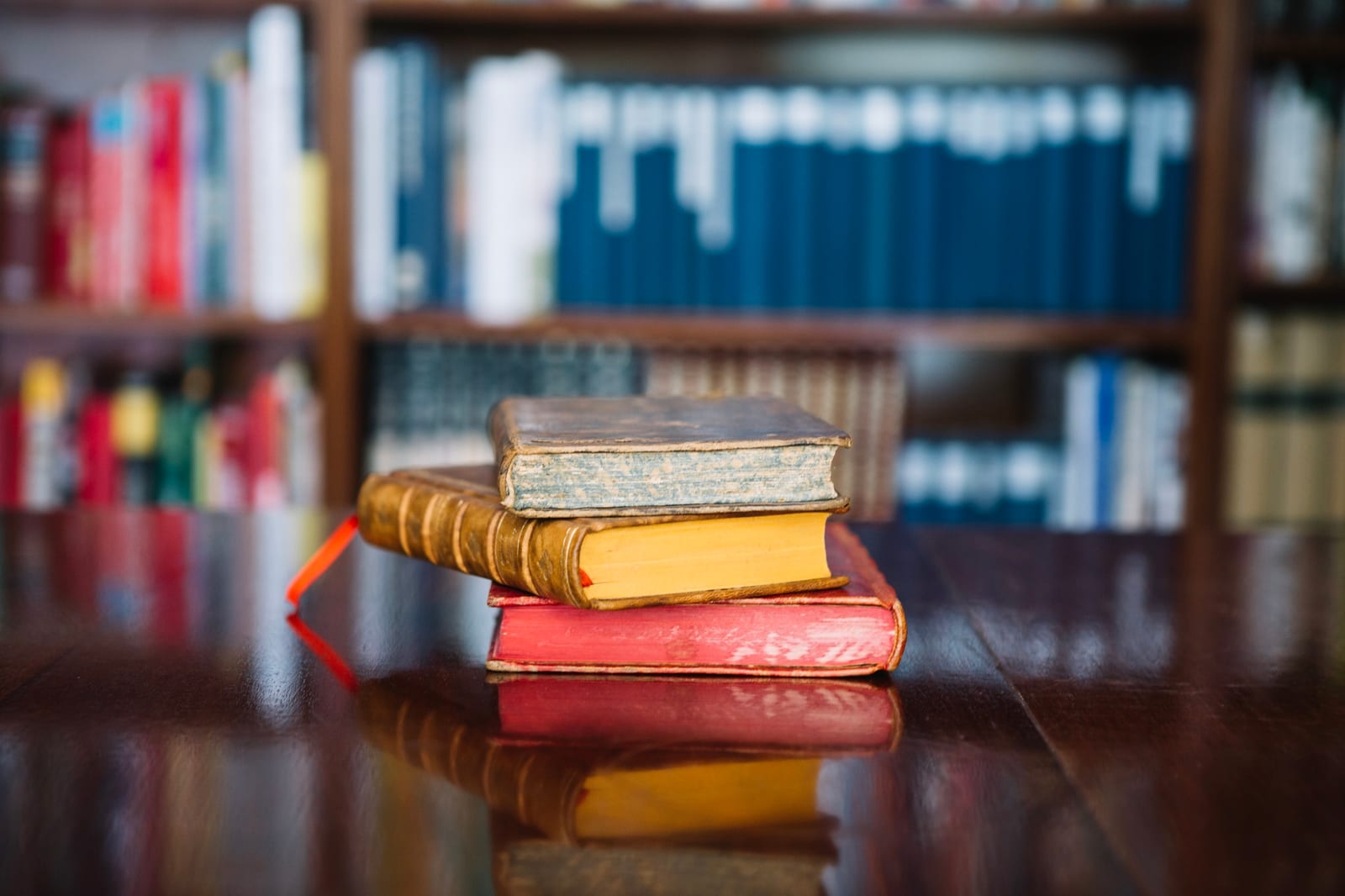 Livros antigos empilhados ao lado de uma vela acesa e uma planta, em uma composição tranquila sobre a mesa